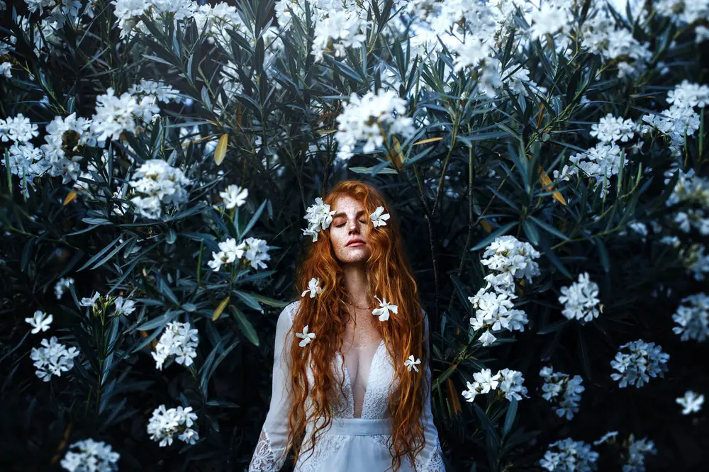 Woman in white dress and white flowers in hair standing in front of white-flowered plants