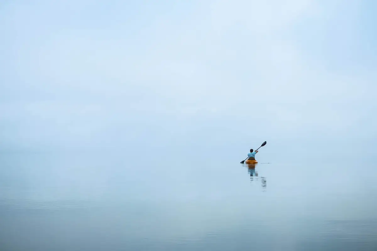 Person rowing a kayak on a calm body of water.