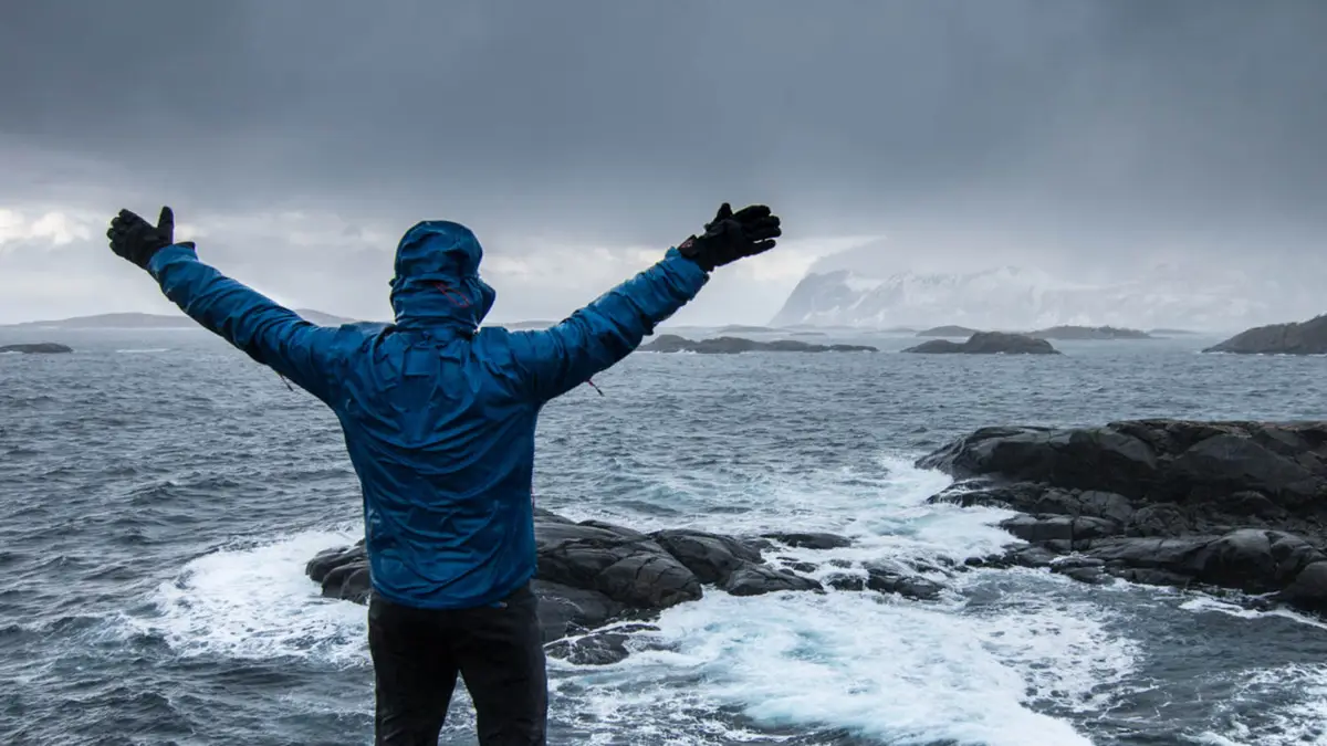 Person in foreground, facing ocean, with far off snowy mountains in the background.