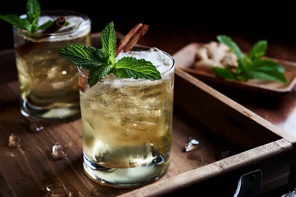 A mint cinnamon drink in focus in foreground, and another drink and ingredients blurred in the background.